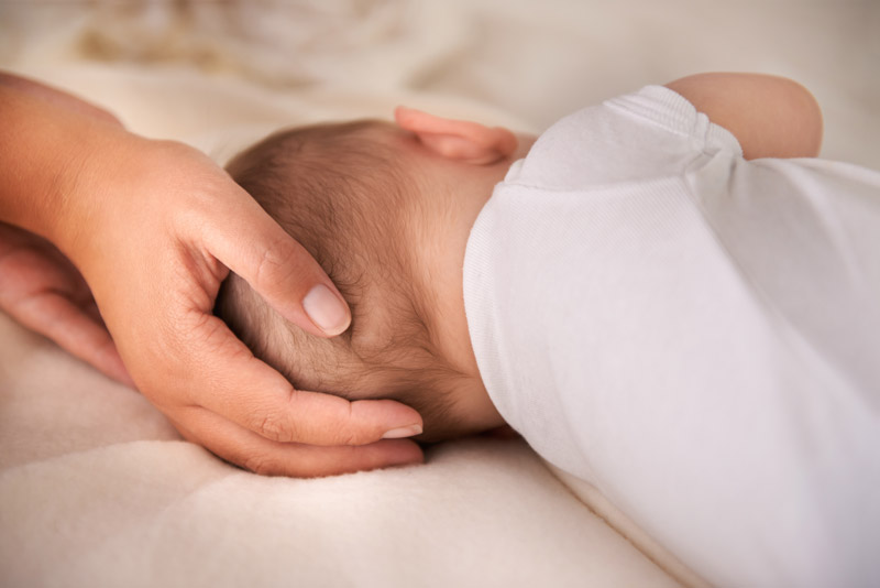 Terapia manuale neonatale: mano che sostiene la testa di un neonato